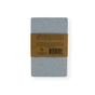 A rectangular gray soap bar, wrapped with a brown paper band showing printed text and a barcode, rests on a white background beside the Me Mother Earth Quick-Dry Diatomite Soap Dish—perfect for keeping your shampoo and conditioner bars fresh and long-lasting.