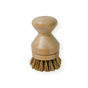 The Me Mother Earth Scrub Brush for Pots and Pans features a short, smooth bamboo handle and stiff plant-based bristles at the bottom for effective cleaning. This plastic-free brush is shown against a white background.
