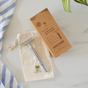The Me Mother Earth Reusable Double Edge Safety Razor sits on a cream pouch next to its brown box, with a striped cloth and green plant nearby—a stylish, eco-friendly solution for zero waste shaving.