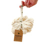 A hand holds a white Reusable Sisal Shower Pouf by Me Mother Earth by its tag, which highlights that it’s made from agave plant fibers, washable, recyclable, and completely plastic-free. This natural exfoliating pouf is an ideal eco-friendly shower accessory for a sustainable clean.