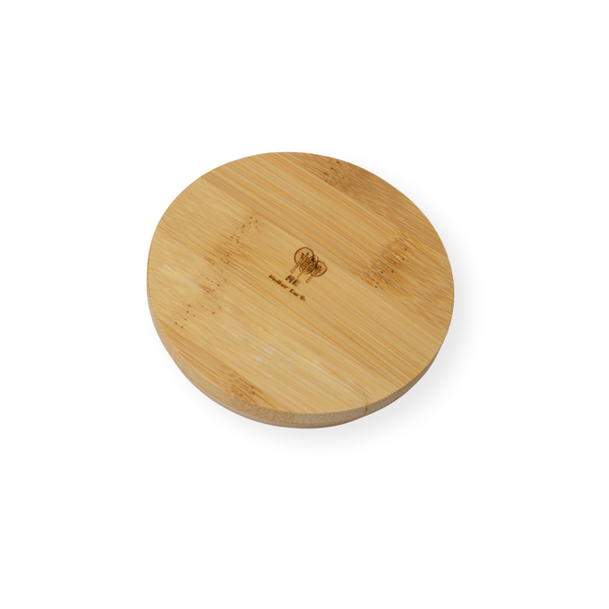 The Me Mother Earth Solid Bamboo Mason Jar Lid features a round design with natural wood grain and a chef’s hat logo engraved at the center, shown on a white background. Ideal as an eco-friendly lid for mason jars.