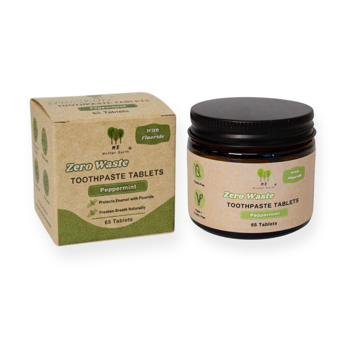 A box and a jar of Me Mother Earth Toothpaste Tablets with Fluoride - Zero Waste, Peppermint flavor, each containing 65 travel-friendly tablets. The plastic-free packaging emphasizes fluoride content and eco-friendly features.