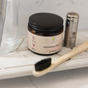 A Me Mother Earth bamboo toothbrush, a glass, a metal container, and fluoride-free Toothpaste Tablets in an Amber Glass Jar are arranged on a bathroom shelf.
