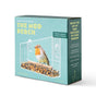 A turquoise box labeled Modern Sprout showcases the Window Bird Feeder—a sleek, window-mounted acrylic feeder featuring a bird perched inside amid scattered seeds. Product features are highlighted in text, and a charming cat illustration decorates the side of the packaging.