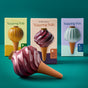 Three colorful boxes labeled "Modern Sprout Watering Bulbs, Variety Pack" stand behind a bulb-shaped ceramic plant waterer with a brown terracotta base and glossy purple swirl top on a teal surface and background.