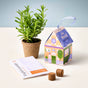 The Home Grown Ornaments kit by Modern Sprout features a small potted plant, an illustrated house-shaped box labeled Grow Peace, a packet of English lavender seeds, and two soil pellets—all elegantly arranged on a light surface to create a delightful grow kit that brings natural beauty to any space.