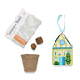 The Home Grown Ornaments kit by Modern Sprout includes a basil seed packet, two soil pellets, a biodegradable pot, and a vibrant house-shaped box topped with a blue ribbon—all beautifully arranged on a white background for an easy and delightful herb-growing experience that doubles as the perfect giftable ornament.