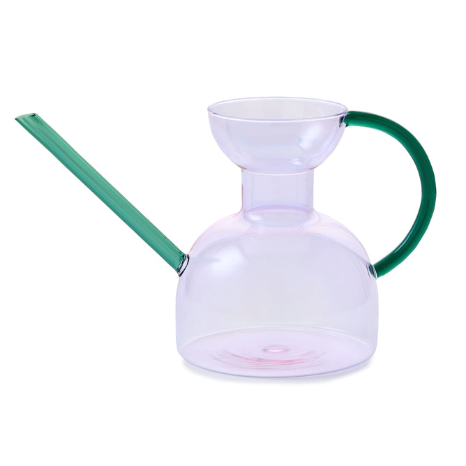 The Modern Sprout Handcrafted Borosilicate Glass Watering Can features a pinkish body, long left-angled green spout, and curved right green handle—ideal for watering or as a unique plant propagation vessel against a white background.