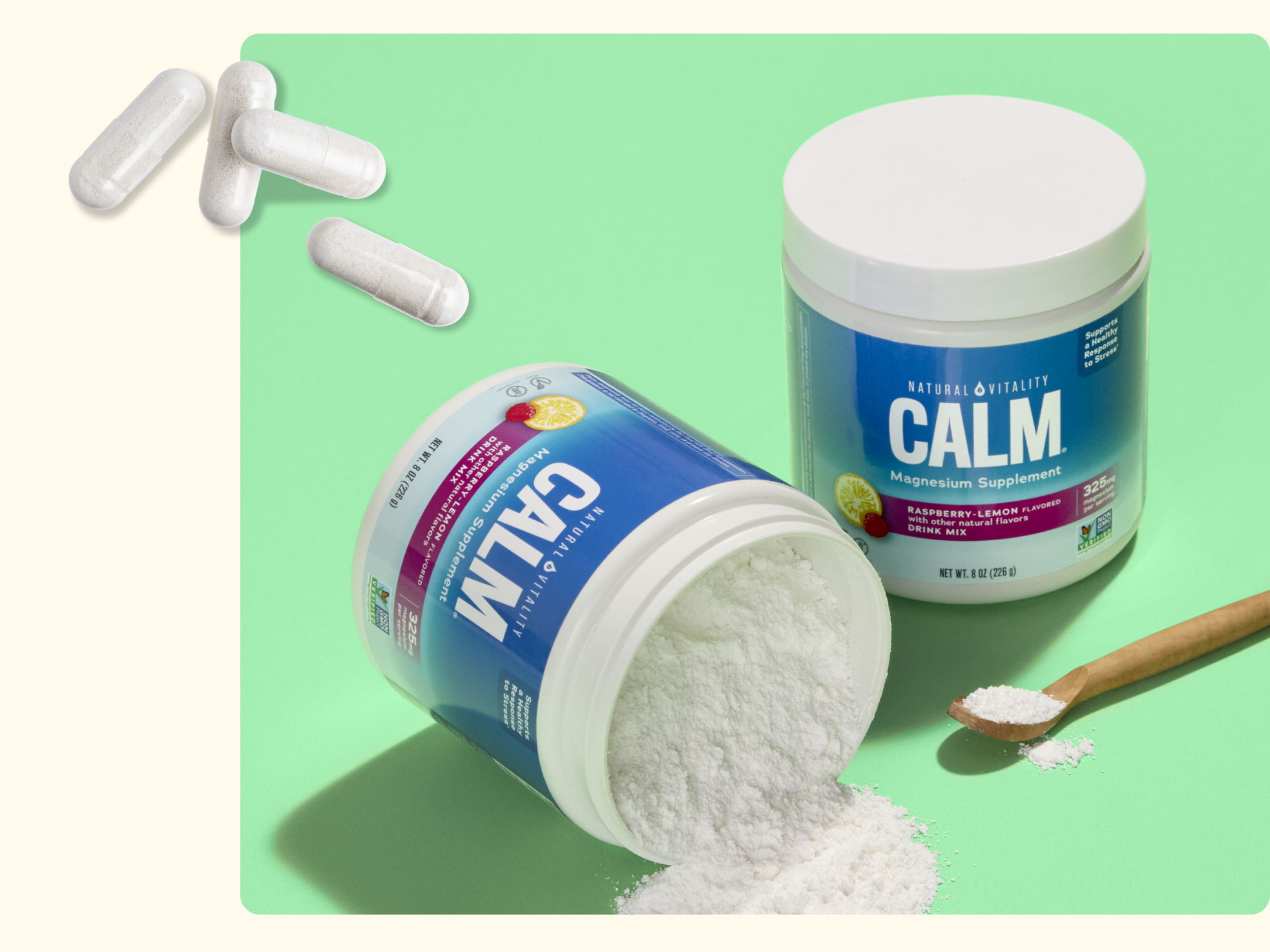 Two containers of CALM magnesium supplement, one upright and one tipped over spilling powder, sit on a green surface. There’s a wooden spoon with powder beside them and three white capsules in the corner.