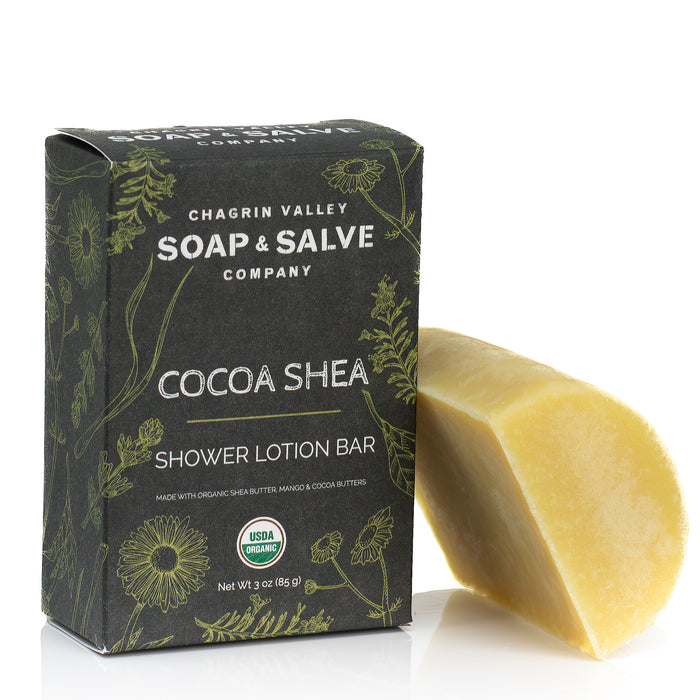A box labeled Chagrin Valley Soap & Salve Shower Butter Bar sits beside an unwrapped, yellowish bar. Made with rich shea and cocoa butters, this after-shower lotion bar helps replenish and nourish dry skin.