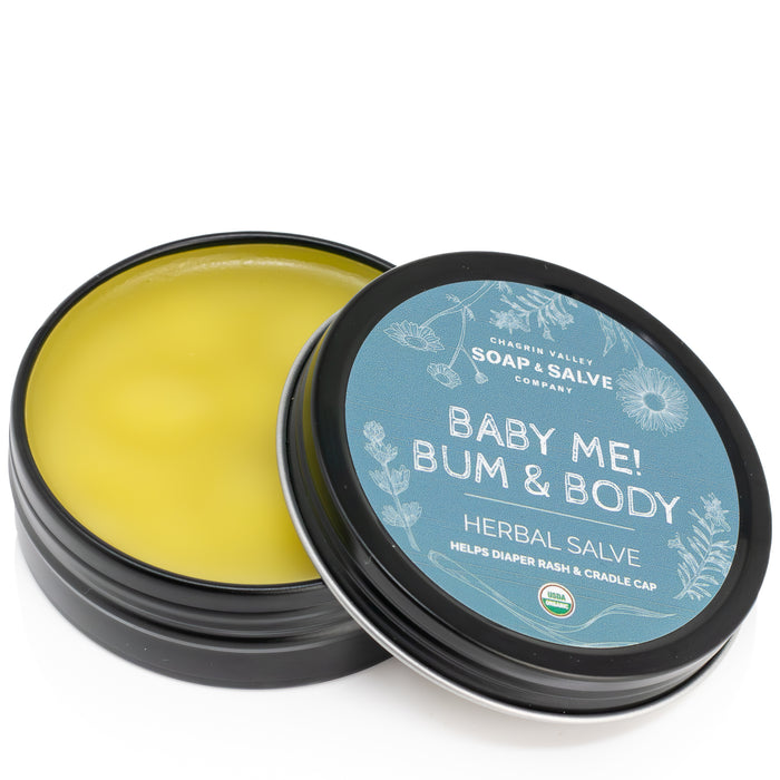 An open tin of yellow Baby Bum Salve by Chagrin Valley Soap & Salve with a black lid, specially formulated to soothe diaper rash and cradle cap.