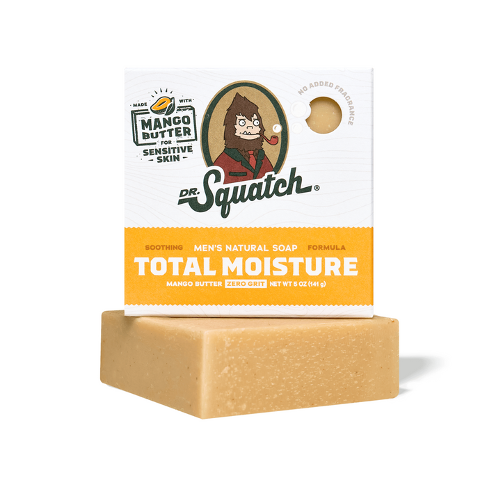 A bar of Dr. Squatch Men's Total Moisture Soap sits in front of its box, featuring natural butters for sensitive skin and zero grit. The packaging shows an illustrated character with orange and green text.