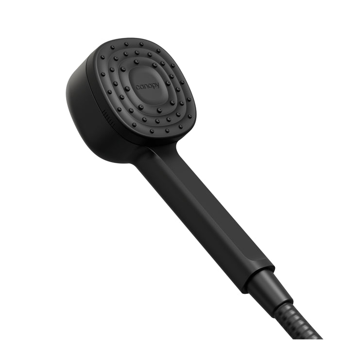 The Canopy Filtered Showerhead features a matte black, modern rectangular handle and a round spray face with small, evenly spaced nozzles. The brand name appears at the center, and its designed to support healthy skin and hair.