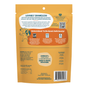 Back of a Shameless Pets Dog Treats - Meat Me At The Feast bag, orange in color, featuring descriptive text, certification logos, an ingredient list, nutrition facts, and a barcode at the bottom. Illustrations include a dog and sweet potatoes.