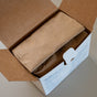 An open cardboard box with outward-folded flaps reveals a sealed brown paper bag of Meliora Laundry Powder Refill, with eco-friendly product details printed on the side.