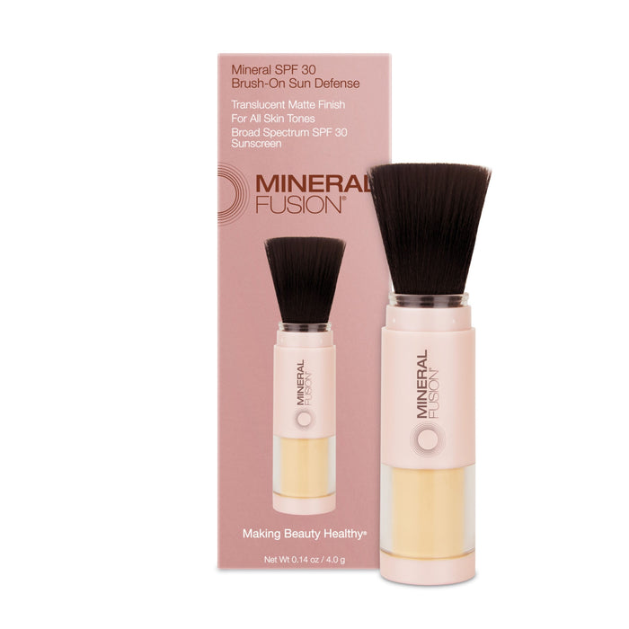 A Mineral Fusion Mineral SPF 30 Brush-On Sun Defense, featuring translucent mineral sunscreen powder and a soft brush, is displayed in front of its pink and brown packaging.