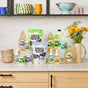 Molly’s Suds Dishwasher Detergent Pods are displayed on a kitchen counter with dishes, flowers in a vase, and bowls on shelves in the background.