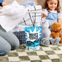 A bag of Molly’s Suds Laundry Detergent Powder rests on a green-and-white checkered rug before a laundry basket with folded clothes, while a child in a blue dress hugs a plush bunny nearby.