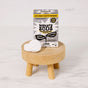 A box of Molly's Suds Washing Machine Cleaner sits on a small wooden stool, with three white tablets in front. The packaging highlights a lemon scent, earth-friendly cleaning, and effective odor removal.