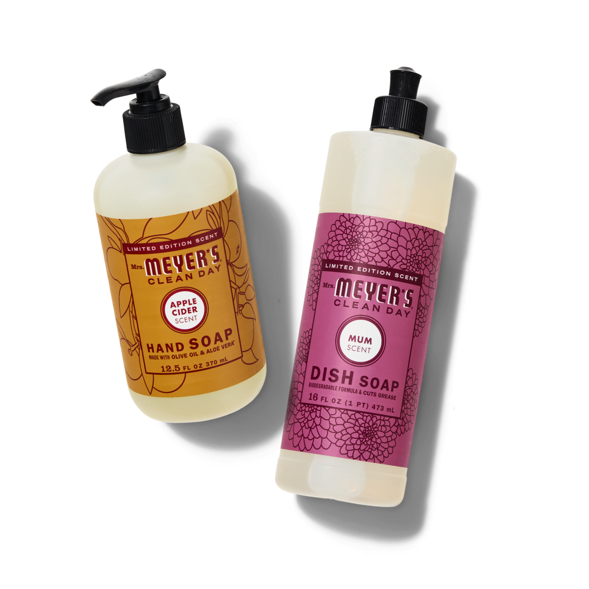 Two bottles of Mrs. Meyer’s Clean Day soaps: a hand soap with apple cider scent in a pump bottle and a dish soap with mum scent in a squeeze bottle, both with colorful floral labels.
