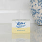 A box of Nellie's Dish Butter Refill, a zero-waste dish soap, rests on a white countertop beside a blue and white floral vase.