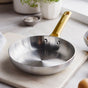 The GreenPan Reserve Stainless Steel Open Fry Pan, featuring a gold-colored handle, rests on a white surface in a bright kitchen with bowls and plants in the background—ideal for achieving restaurant-quality results.