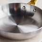 Close-up of the GreenPan Reserve Stainless Steel Open Fry Pan with a golden handle, resting on a light surface. The sleek, tri-ply design reflects light on its smooth interior—ideal for restaurant-quality cooking.