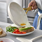 Someone uses the GreenPan Reserve Pro Open Frypan, a beige ceramic nonstick pan with a gold handle, to cook a sunny-side-up egg and place it onto toast with avocado, arugula, and cherry tomatoes in a modern kitchen.