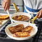 Wearing a white shirt and blue apron, a person cooks three slices of French toast in a GreenPan Reserve Pro Frypan on the stove, while another GreenPan skillet with fruit compote sits on the back burner.