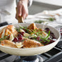 A person sautés seasoned chicken with grapes, garlic, and rosemary in the GreenPan Reserve Pro Frypan Set on the stovetop, with steam rising as the PFAS-free hard anodized pans capture a moment of healthy cooking.