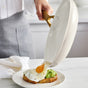 In a bright kitchen, someone slides a sunny-side-up egg from the GreenPan Reserve Pro Cookware Set’s PFAS-free ceramic nonstick pan onto avocado toast on a white plate.