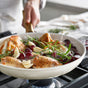A person sautés chicken, garlic, grapes, and rosemary in a GreenPan Reserve Pro Cookware Set PFAS-free ceramic nonstick skillet on a gas stove. Steam rises from the pan as the flavors blend together.