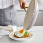 A person slides a fried egg from the GreenPan Reserve Pro Cookware Set onto avocado toast on a white plate, arranged on a marble countertop in a bright kitchen.
