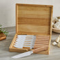 The GreenPan Elite Light Pakka Wood Steak Knife Boxed Set, open on a kitchen counter, displays eight ergonomic steak knives. Garlic and rosemary nearby highlight the precision-cut blades—ideal for any meal prep.
