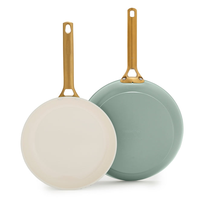 Two GreenPan Reserve Pro Frypans stand upright with gold handles; one cream pan faces forward, while the sage green pan displays its bottom.