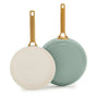 Two GreenPan Reserve Pro Frypans stand upright with gold handles; one cream pan faces forward, while the sage green pan displays its bottom.