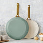 The GreenPan Reserve Pro Frypan Set features two PFAS-free frying pans—one mint green and one cream with gold handles—crafted from hard anodized aluminum, shown against a white tiled kitchen backsplash for safe, stylish cooking.