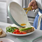 A person slides a fried egg from a GreenPan Reserve Pro Frypan onto toast with avocado, greens, and cherry tomatoes on a white plate set on a kitchen counter.