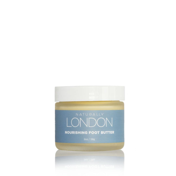A small glass jar of Naturally London Nourishing Foot Butter with a light blue label and white lid, featuring cupuaçu, mango, and avocado butters, shown against a clean white background.