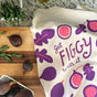 A kitchen scene features The Neighborgoods Dish Towel Set with a fig design and “Get Figgy With It” text, fresh figs, rosemary on a wooden board, and a white bowl of figs atop a granite countertop.