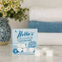 A box of Nellie's Laundry Cubes, 16 Load, rests on a counter beside four white, PVA-free cubes. A vase of daisies and two folded towels in the background accentuate the clean, planet-friendly vibe.