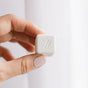 A hand with light pink nail polish holds a Nellie's Laundry Cube, highlighting its PVA-free, planet-friendly formula. The small, white, square tablet with a raised 