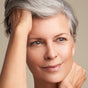 A woman with short gray hair smiles softly, her calm confidence and clear skin suggesting she uses a plastic-free hair care routine like The Detoxifier Conditioner by NOTICE Hair Co.