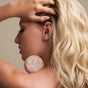 A woman with long blonde hair holds The Fixer Shampoo bar by NOTICE Hair Co against her neck and shoulder, showcasing plastic-free hair care, as her other hand rests on her head in front of a neutral background.