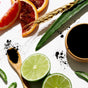 Sliced limes, blood orange, activated charcoal, aloe vera leaves, and wheat on a white background—fresh inspiration for The Detoxifier Shampoo by NOTICE Hair Co, your go-to clarifying treatment and gentle detox shampoo bar.