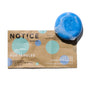 A blue Kids Shampoo Bar - For Tangles from NOTICE Hair Co sits on brown and blue packaging, designed for detangling and fine hair, with suds visible.