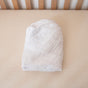 A neatly folded white blanket rests on a crib mattress beside wooden rails, highlighting Naturepedic Organic Breathable Muslin Crib Sheets for a cozy, natural nursery.