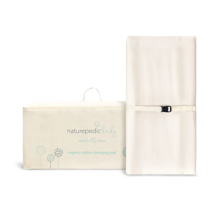 The Naturepedic Organic Cotton Changing Pad stands upright beside its cream carrying case, which has a handle and minimalist tree designs. Size: 16.5 x 31.5 x 4 inches.