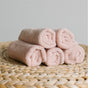 Five soft, pink Natemia Organic Super Absorbent Washcloths, made from 100% GOTS Certified Organic Cotton, are rolled and stacked in a pyramid on a woven natural-colored surface with a plain light background.