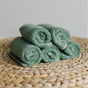 Six rolled Natemia Organic Super Absorbent Washcloths, made from 100% GOTS Certified Organic Cotton, are neatly stacked in two rows on a woven circular mat against a light background.